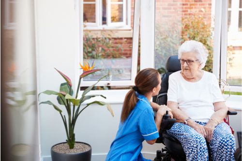 A care assistant kneels before an elderly woman